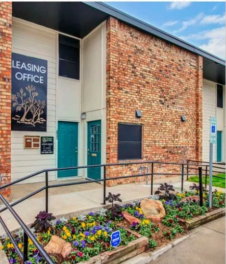 Leasing office entrance with a Leasing Office sign, teal doors, a handrail along the walkway, and a flower bed of pansies in front.